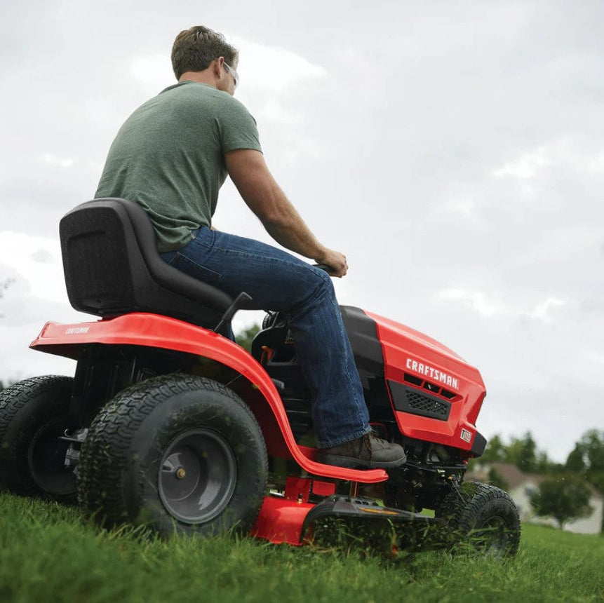 Man operating a red Craftsman riding lawn mower on grass with a cloudy sky.